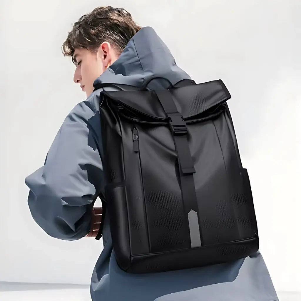 Man in grijsblauwe jas met zwarte 17 inch laptop rugzak. Waterafstotend rolltop-design voor alle weersomstandigheden.