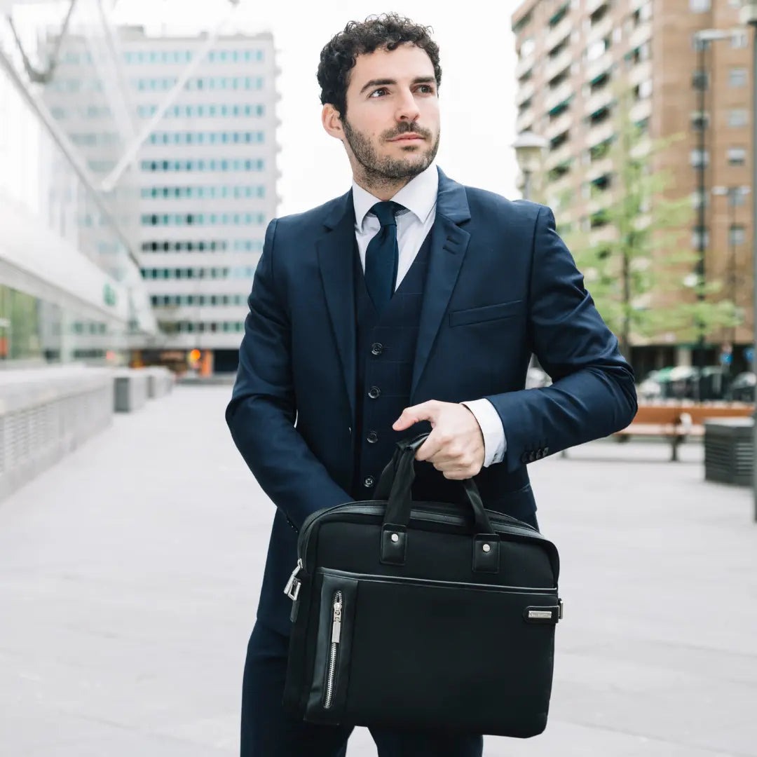 Zakenman in blauw pak met zwarte laptoptas in stedelijke omgeving.