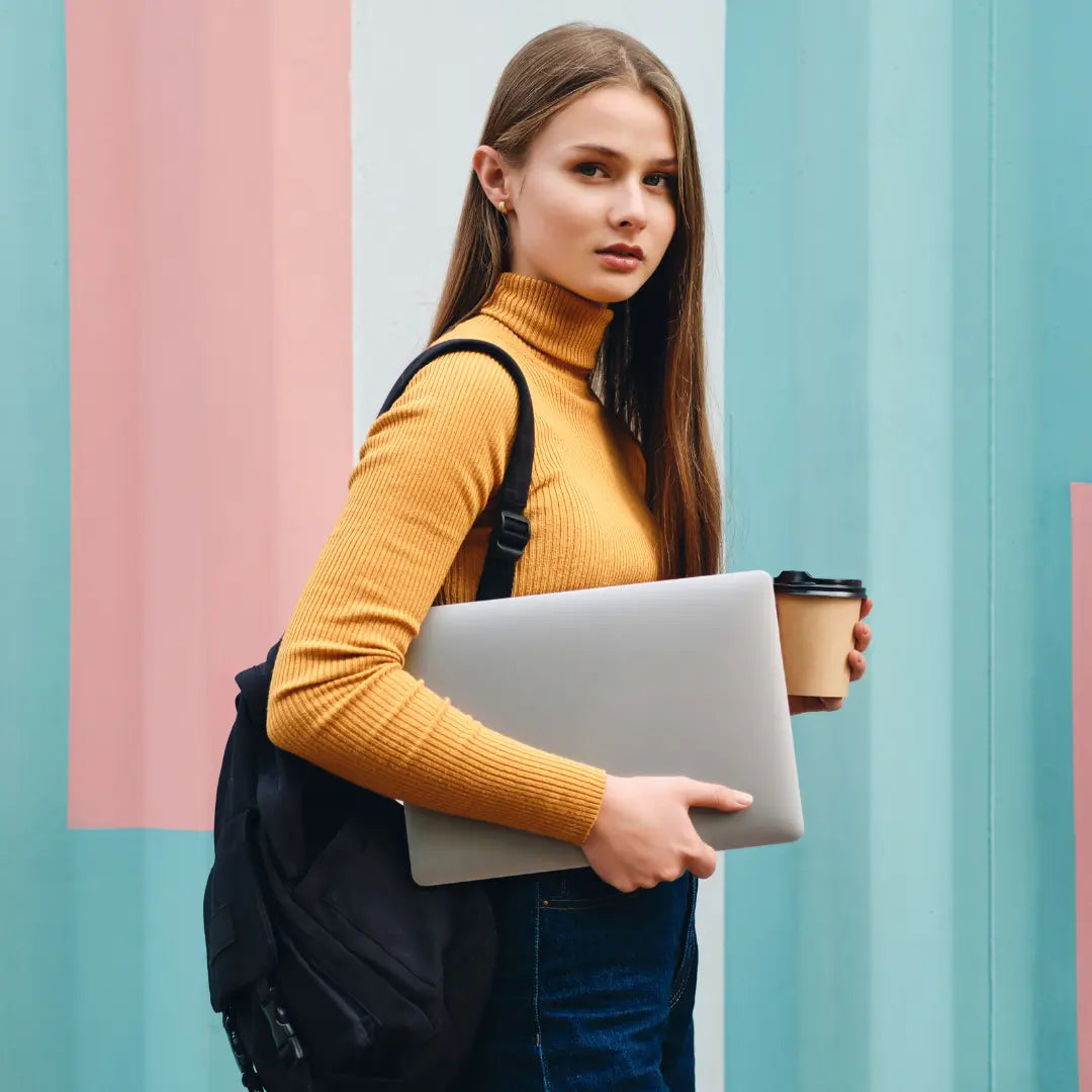 Student met oranje coltrui en zwarte laptop rugzak draagt laptop.