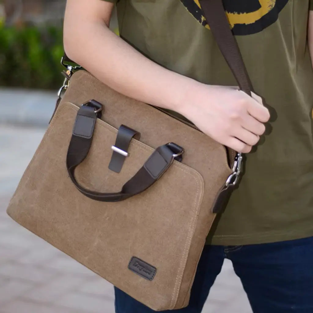 Canvas laptoptas heren gedragen aan schouderriem door persoon in groene shirt, laat de praktische draagbaarheid zien.