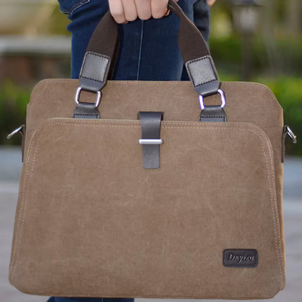 Canvas laptoptas heren gedragen in de hand door persoon in jeans, laat de bruine canvas afwerking en leren handgrepen zien.