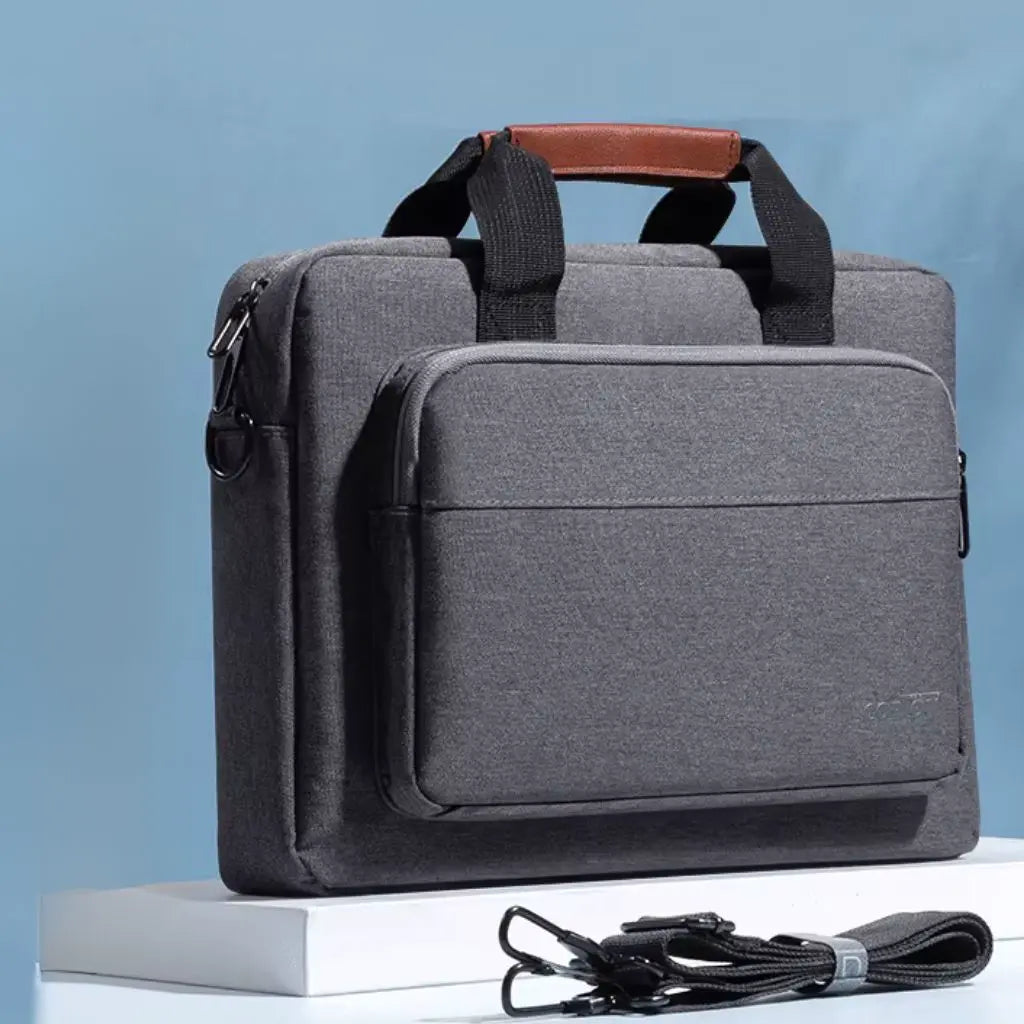 Premium design laptoptas heren donkergrijs getoond tegen een blauwe achtergrond met bijbehorende schouderband. De tas heeft een stijlvolle bruin lederen handgreep, minimalistisch design met functionele vakken en het COPTOT logo subtiel verwerkt in het ontwerp.