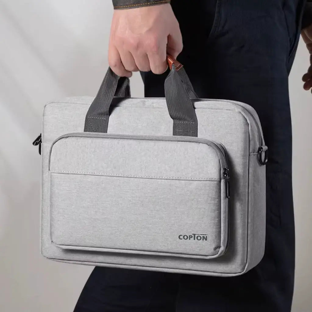 Design laptoptas heren lichtgrijs vastgehouden aan de handgreep door een persoon in donkere kleding. De tas toont de kenmerkende grijze stof, zwarte handgrepen en het COPTON logo, perfect voor dagelijks zakelijk gebruik.