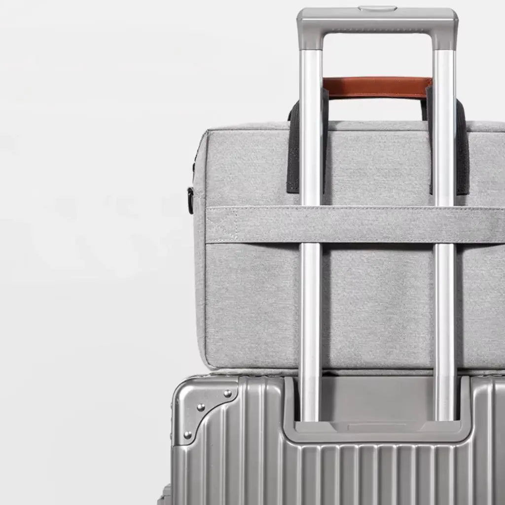 Design laptoptas heren lichtgrijs bevestigd aan een trolleykoffer via de speciale band aan de achterkant. De afbeelding demonstreert de reisfunctionaliteit waarmee de COPTON tas eenvoudig over de handgreep van rolkoffers kan worden geschoven voor moeiteloos reizen.