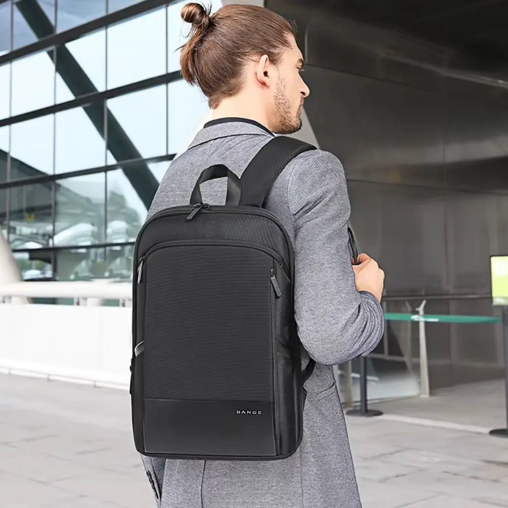 Een man in een grijs pak draagt een dunne waterdichte laptop rugzak van 13 inch, ideaal voor zakelijk gebruik en dagelijks woon-werkverkeer.