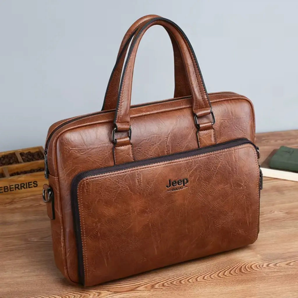 Exclusieve laptoptas heren 14 inch bruin geplaatst op een houten bureau. De bruine lederen tas met Jeep-embleem heeft een stijlvol design met contrasterende zwarte details, metalen bevestigingspunten voor de handgrepen en een klassieke zakelijke uitstraling.