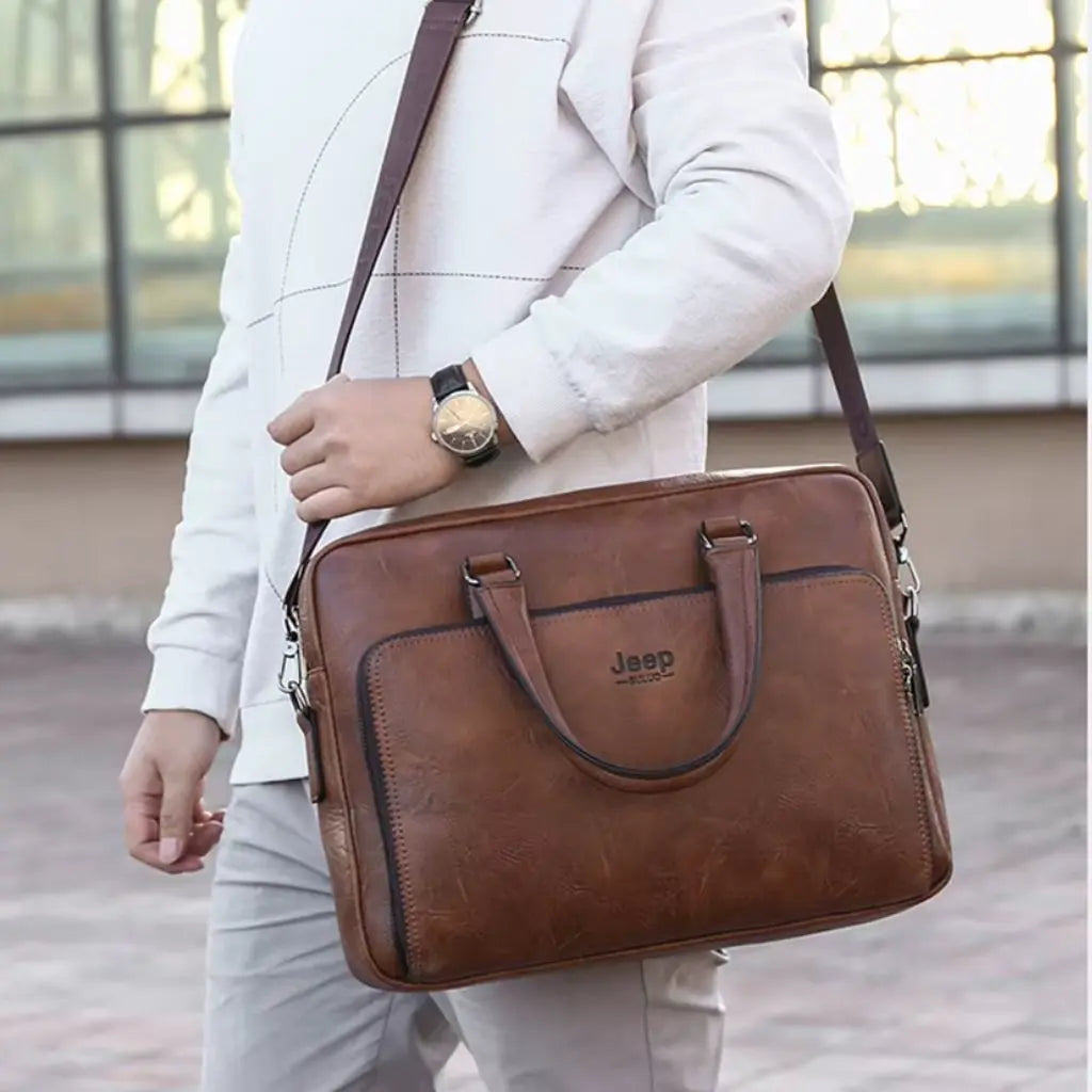 Exclusieve laptoptas heren 14 inch bruin gedragen door een man in wit pak. De bruine laptoptas met Jeep-logo heeft een professionele uitstraling met elegante lederen handgrepen, verstelbare schouderriem en stijlvolle details die perfect passen bij formele zakelijke outfits.