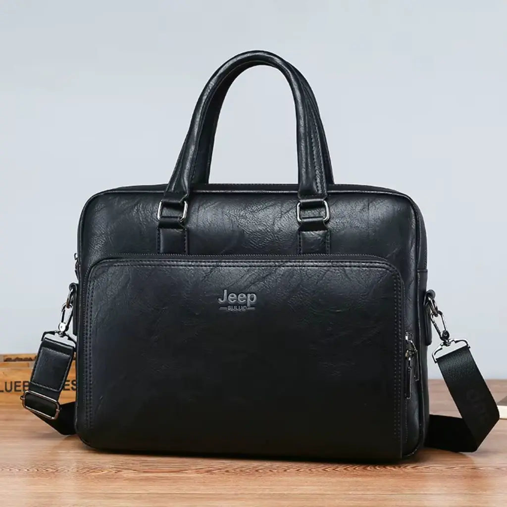 Exclusieve laptoptas heren 14 inch zwart geplaatst op een houten bureau. De zwarte lederen tas met Jeep-embleem heeft een stijlvol design met zilverkleurige details, metalen bevestigingspunten voor de handgrepen en een klassieke zakelijke uitstraling.