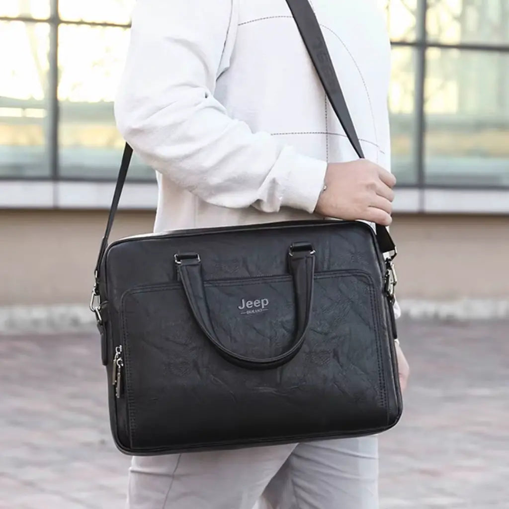 Exclusieve laptoptas heren 14 inch zwart gedragen door een man in wit pak. De zwarte laptoptas met Jeep-logo heeft een professionele uitstraling met elegante lederen handgrepen, verstelbare schouderriem en stijlvolle details die perfect passen bij formele zakelijke outfits.