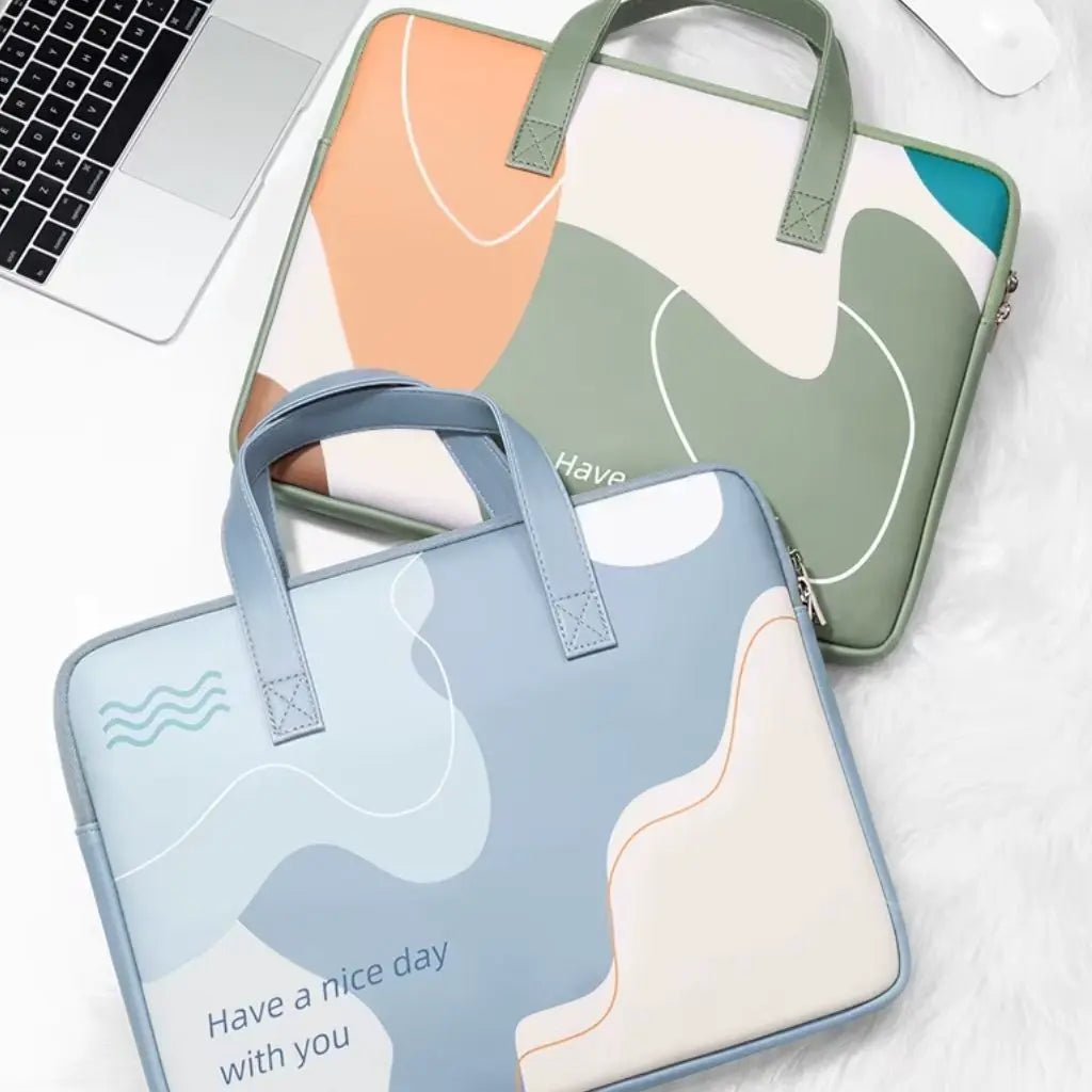 Twee gekleurde laptoptassen op een wit bureau naast een MacBook. De complementaire designs in mintgroen en lichtblauw met abstracte patronen tonen beide de tekst "Have a nice day with you" en bieden een stijlvolle bescherming voor diverse laptopmodellen.
