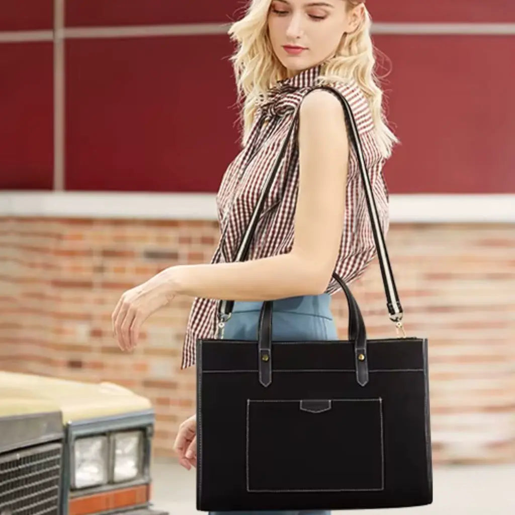 Een jonge vrouw met blond haar draagt een zwarte canvas laptoptas dames 15.6 inch over haar schouder. Ze heeft een geruite blouse aan en de canvas laptoptas dames 15.6 inch past perfect bij haar moderne uitstraling.