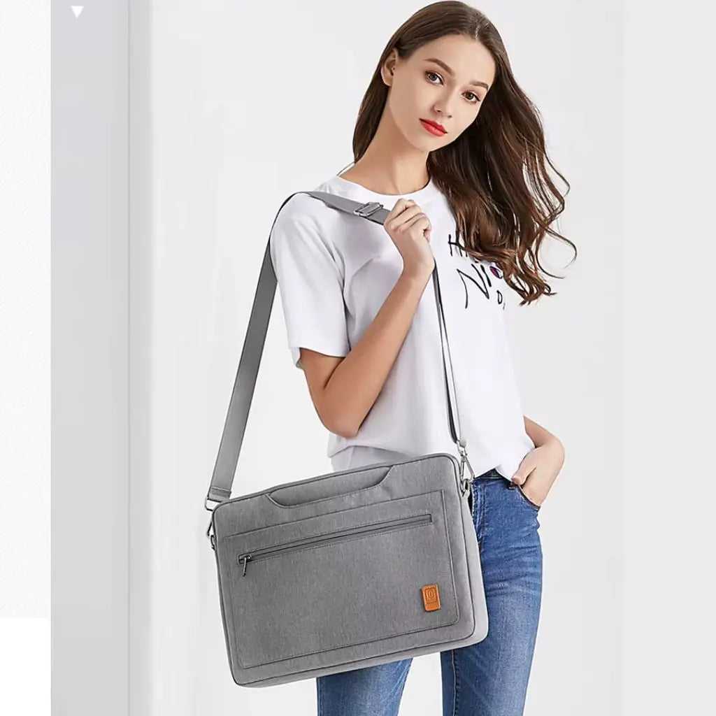 Jonge vrouw draagt een laptoptas dames 16 inch grijs over de schouder, gekleed in een wit t-shirt en jeans, toont de praktische draagbaarheid van de tas met verstelbare schouderriem.