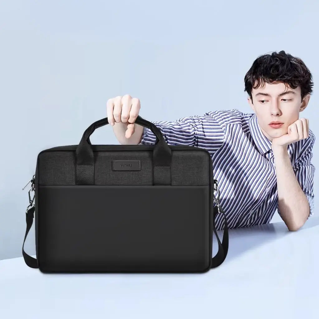 Jonge man in gestreept overhemd houdt de ergonomische laptoptas heren 15.6 inch zwart vast tegen een lichtblauwe achtergrond. De moderne zwarte tas met WIWU-label toont een combinatie van textiel en kunstleer in een minimalistisch design.