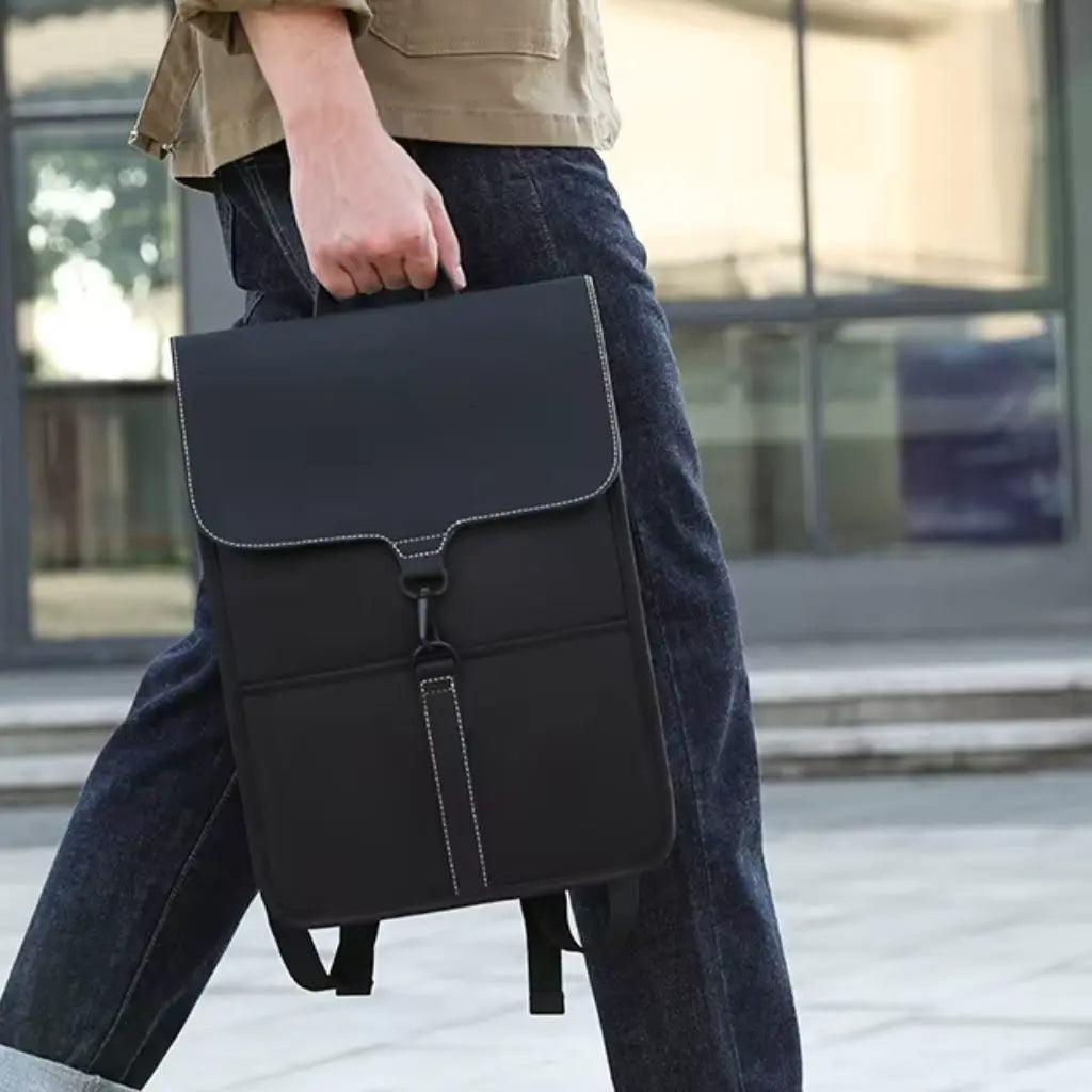 Man loopt met een zwarte rugzak voor laptop 15,6 inch in zijn hand, met stevige leren handvatten en een minimalistisch design. De rugzak oogt professioneel en praktisch.