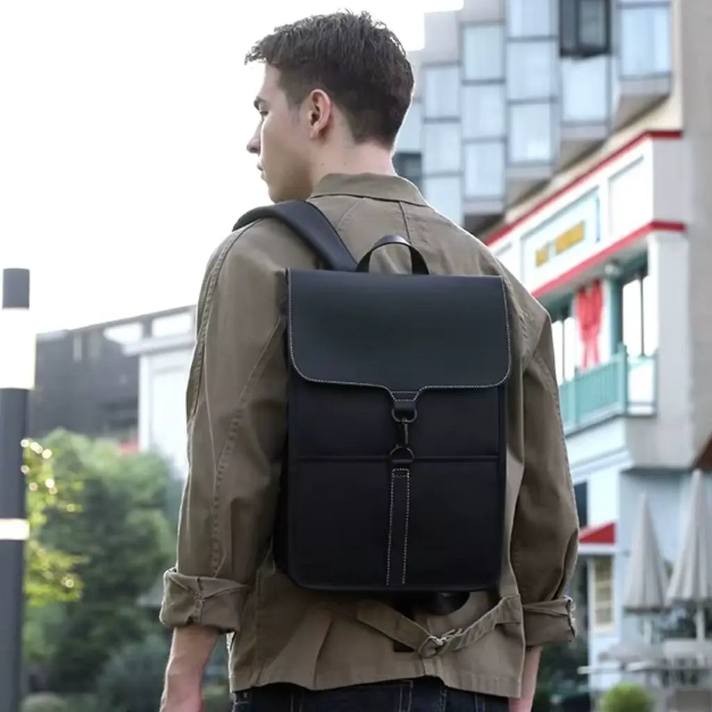 Jonge man met een moderne zwarte rugzak voor laptop 15,6 inch, lopend door een stedelijke omgeving. De rugzak heeft een slank ontwerp met dubbele schouderbanden voor extra comfort.
