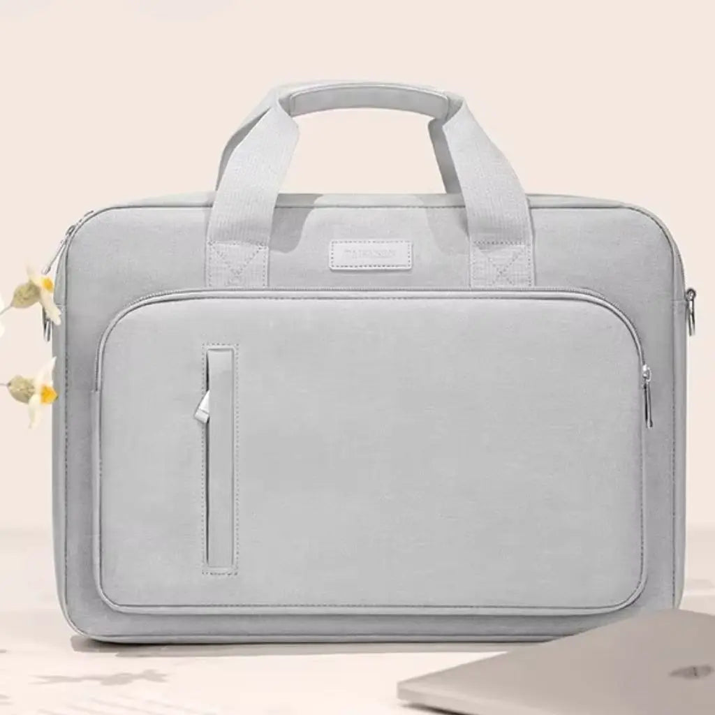 Vooraanzicht van een lichtgrijze kleurige laptoptas dames met een minimalistisch ontwerp en praktisch voorvak. De kleurige laptoptas dames grijs toont de verfijnde afwerking met zilverkleurige ritsen en gewatteerde bescherming, ideaal voor dagelijks gebruik naar kantoor of universiteit.