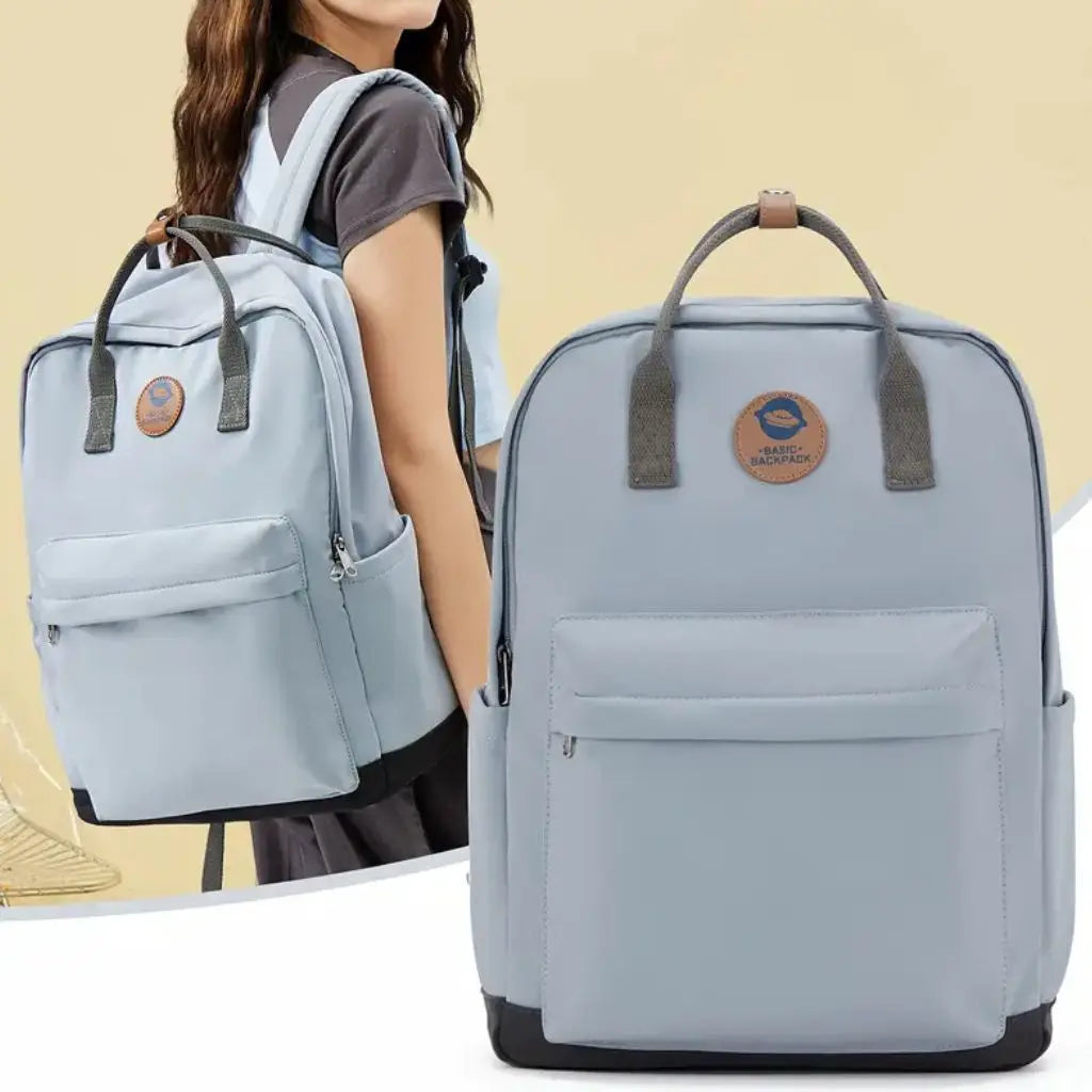 Een laptop rugzak 14 inch meiden blauw getoond op een model en apart afgebeeld, met de kenmerkende lichtblauwe kleur, grijze handgrepen en het Basic Backpack logo, ideaal voor studenten en jonge professionals.