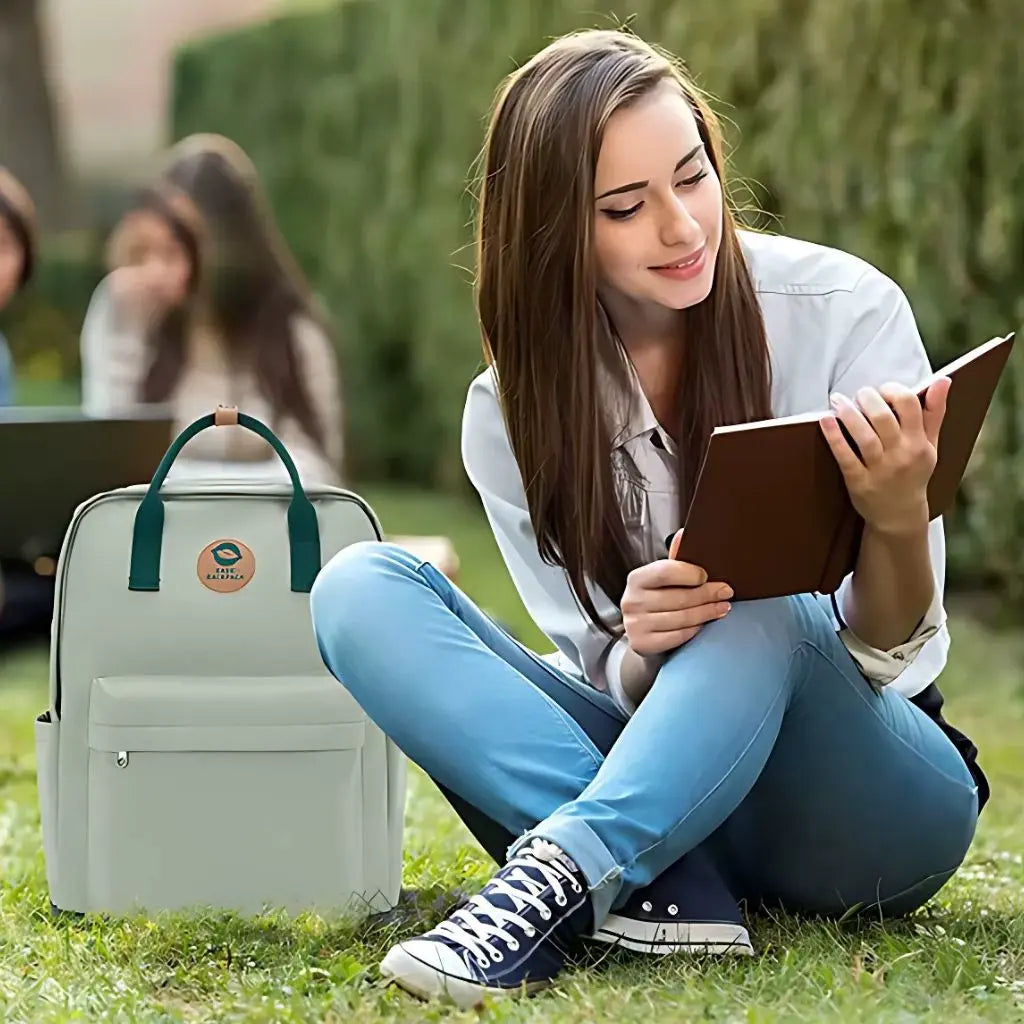 Meisje leest een boek in een park met een groene laptop rugzak 14 inch naast haar. Perfecte rugzak voor studenten of casual gebruik.