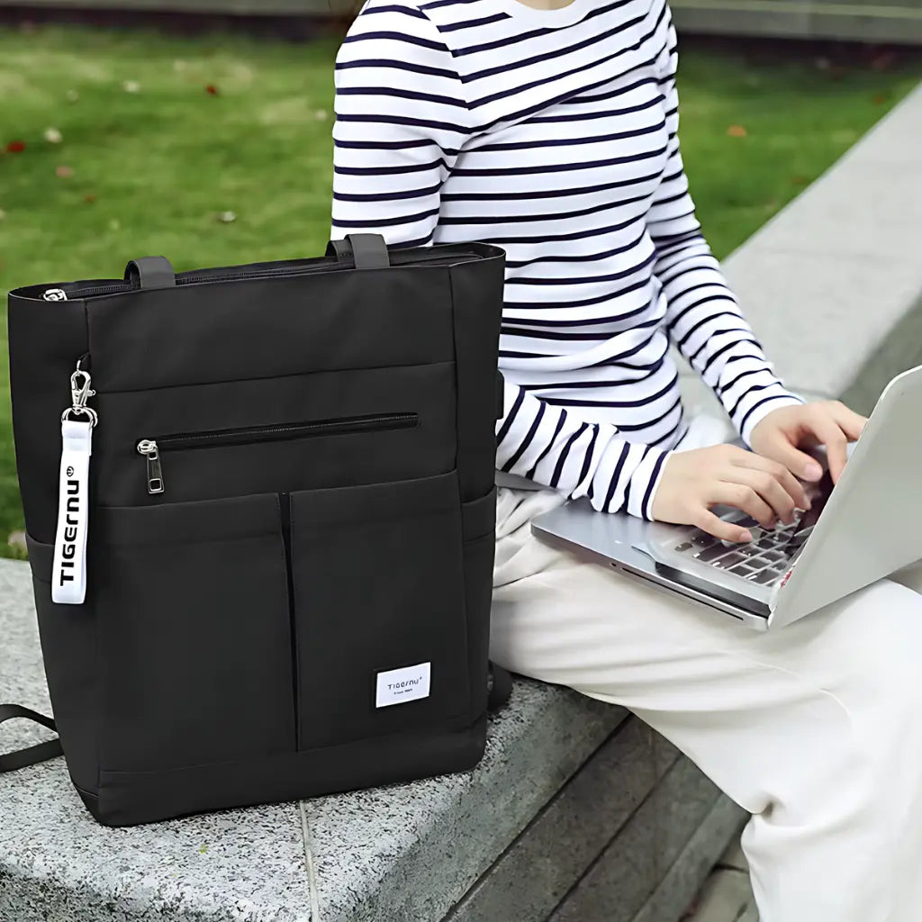 Vrouw gebruikt een laptop naast een laptop rugzak dames 15.6 inch zwart, ideaal voor werk en studie.