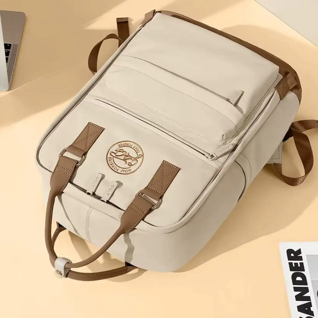 Bovenaanzicht van de laptop rugzak dames 16 inch in crèmekleur op een beige ondergrond. De foto toont de gedetailleerde stiksels, het GOLF-logo embleem en de bruine lederen handgrepen, wat de hoge kwaliteit en het vakmanschap van deze rugzak benadrukt.