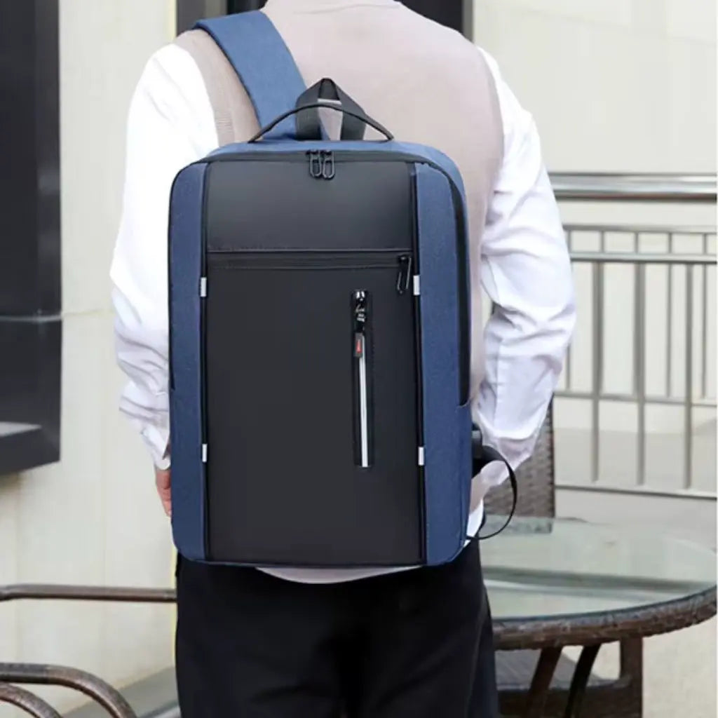 Een model draagt een laptop rugzak heren 15.6 inch compact blauw, wat het draagcomfort en de pasvorm demonstreert. De persoon heeft een wit overhemd aan en de rugzak toont een goede pasvorm op de rug. Het zwarte middenpaneel met reflecterende rits contrasteert mooi met de blauwe zijpanelen, wat een stijlvolle uitstraling geeft voor zowel zakelijke als casual outfits.