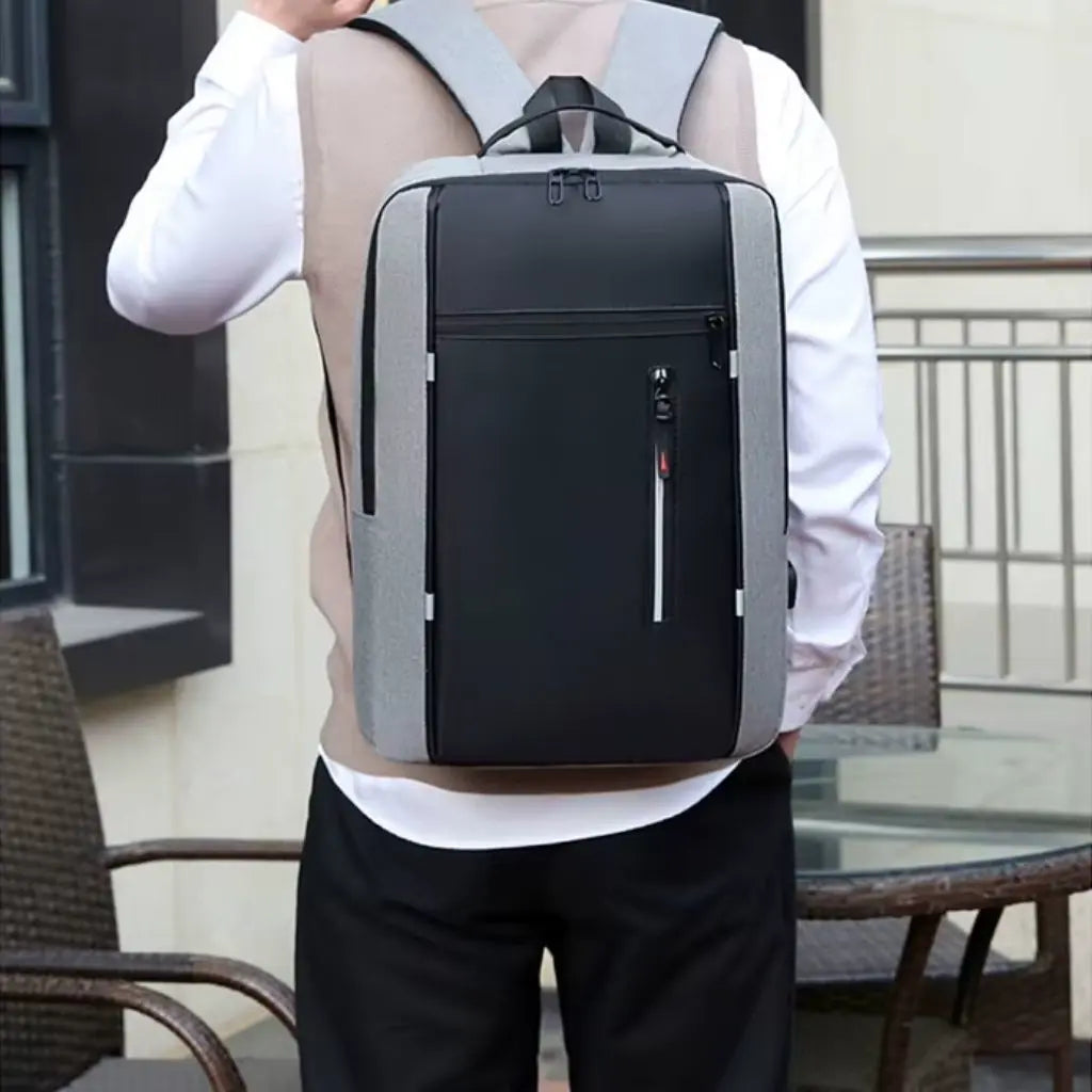 Een model draagt de laptop rugzak heren 15.6 inch compact grijs op zijn rug, wat het draagcomfort en de pasvorm demonstreert. De rugzak zit stevig op de rug en past goed bij zakelijke kleding. Het slanke design maakt de tas ideaal voor woon-werkverkeer, zakenreizen of dagelijks gebruik.