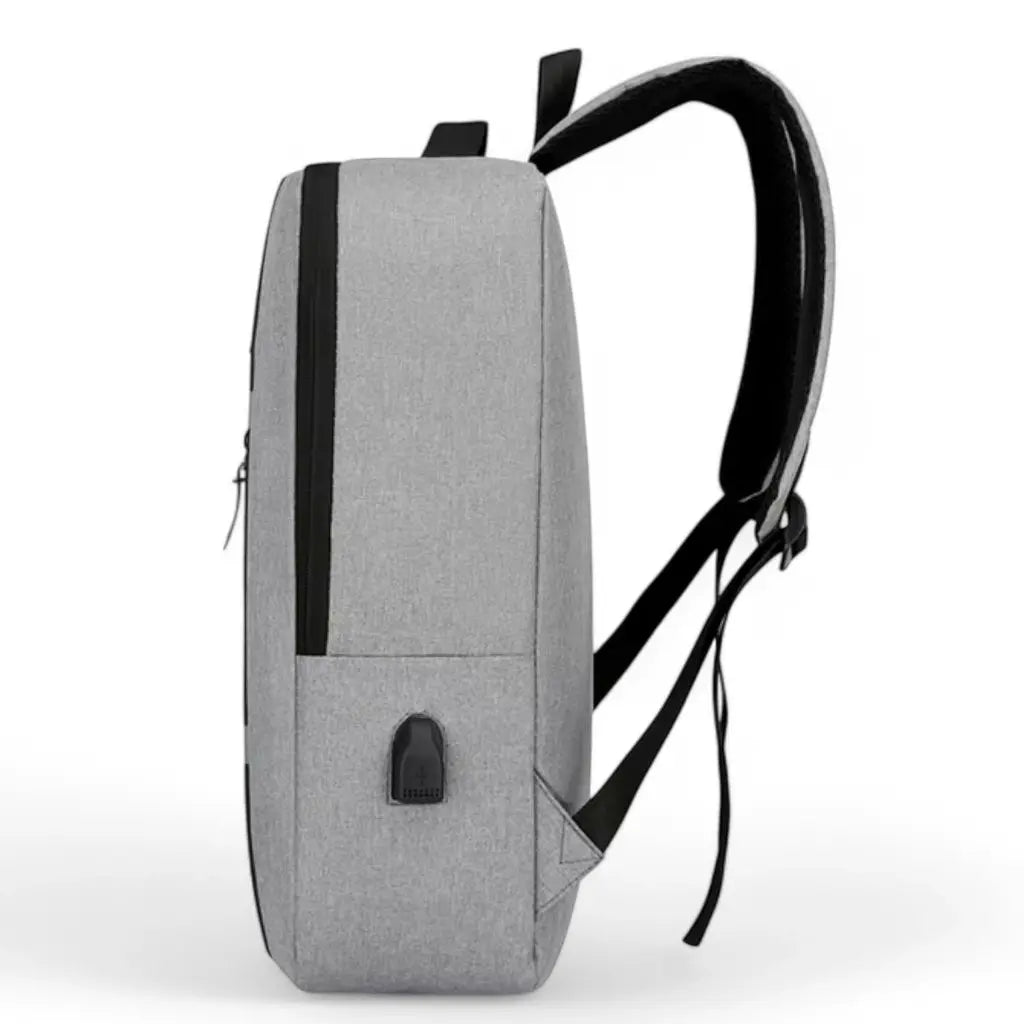 Een laptop rugzak heren 15.6 inch compact grijs vanaf de zijkant gefotografeerd. De rugzak toont de slanke vormgeving met zwarte schouderbanden en een USB-oplaadpoort aan de zijkant. Het lichtgrijze textielmateriaal is duurzaam en waterafstotend, ideaal voor dagelijks gebruik in verschillende weersomstandigheden.