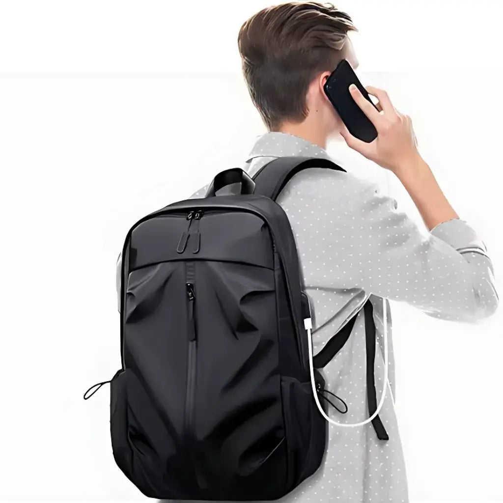 Man in grijs overhemd die telefoneert terwijl hij een laptop rugzak heren 17 inch draagt, wat de veelzijdigheid toont van deze rugzak voor zakenreizigers en professionals die een betrouwbare laptop rugzak heren 17 inch zoeken.