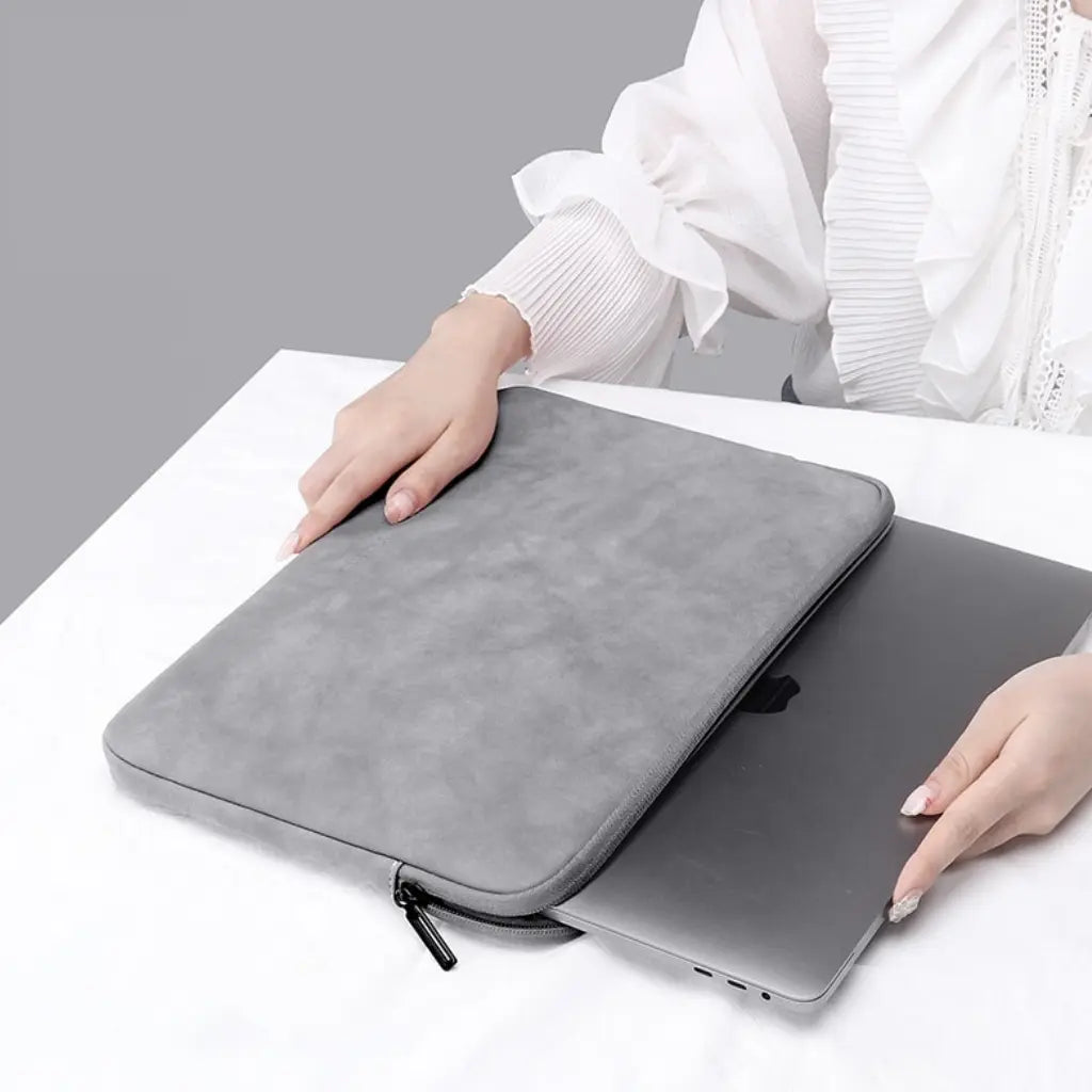 Persoon die een grijze laptop sleeve 14 inch vasthoudt op een witte tafel, toont gebruiksvriendelijkheid