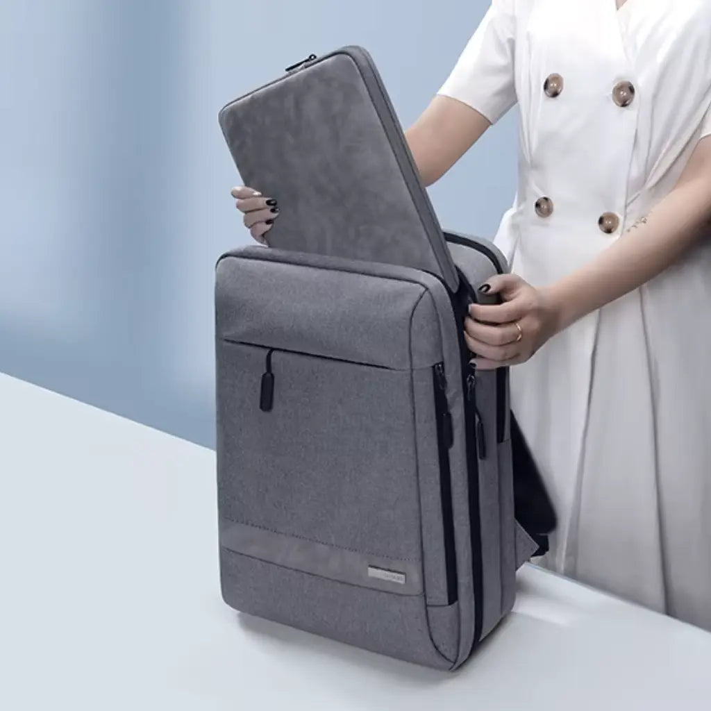 Grijze laptop sleeve 14 inch wordt uit een bijpassende rugzak gehaald door een persoon in witte kleding
