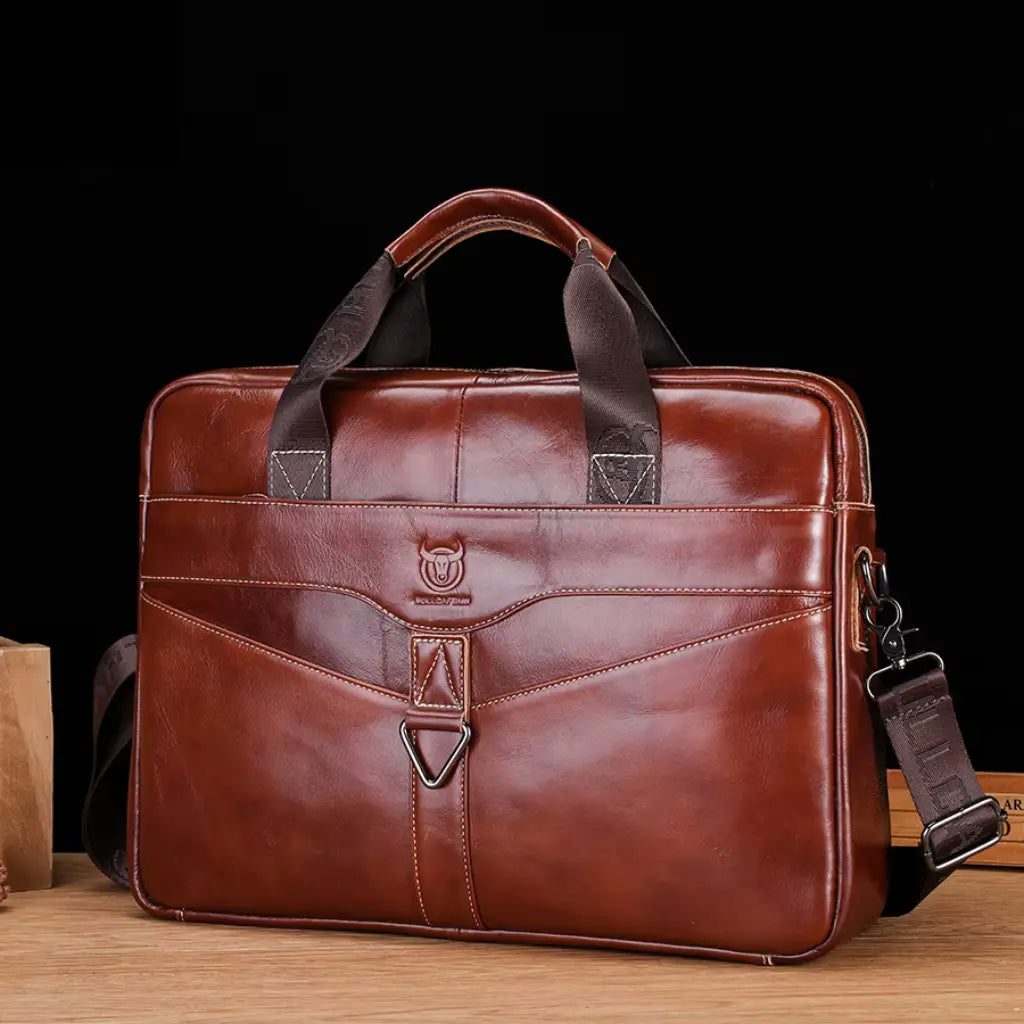 Laptoptas cognac heren 15 inch gefotografeerd tegen zwarte achtergrond, toont de hoogwaardige leren afwerking en het logo op de voorkant.