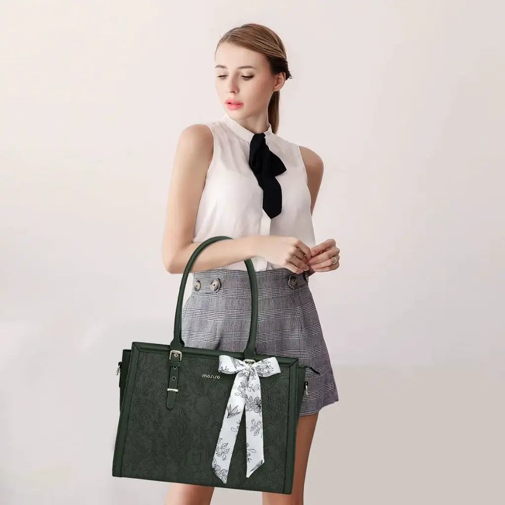 Een stijlvolle jonge vrouw in een witte blouse met zwarte strik en grijze geruite rok draagt de laptoptas dames 15.6 inch groen met decoratief lint. De donkergroene laptoptas dames 15.6 inch groen past perfect bij haar zakelijke look.