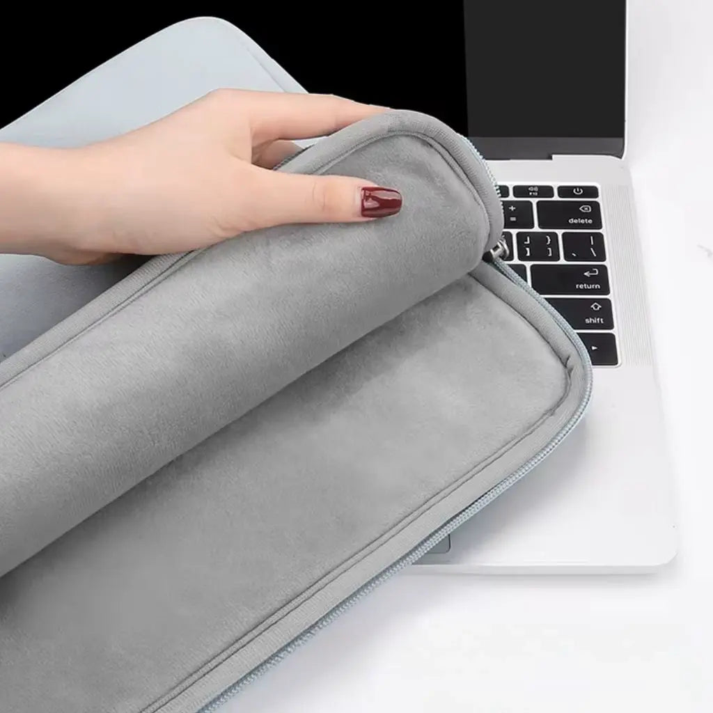 Close-up van de laptoptas dames klein grijs die wordt geopend om de zachte binnenvoering te tonen. Een hand met rode nagellak opent de ritssluiting, waarmee de beschermende binnenkant zichtbaar wordt die perfect is voor het veilig transporteren van elektronische apparaten.