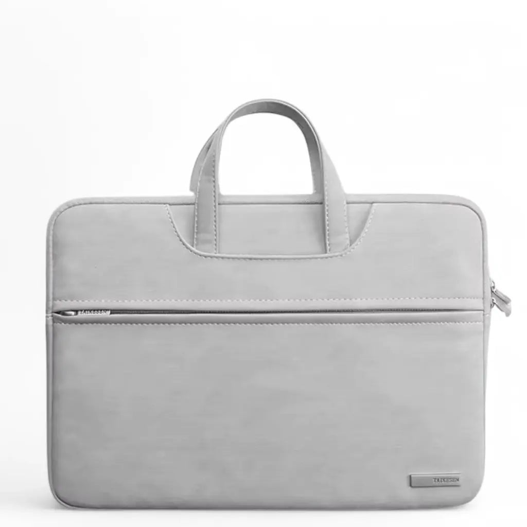 Stijlvolle laptoptas dames klein grijs met handvaten en een voorvak met ritssluiting. De compacte, lichtgrijze tas heeft een minimalistisch design met subtiel TAIKESEN merklogo, perfect voor dagelijks gebruik of werk.