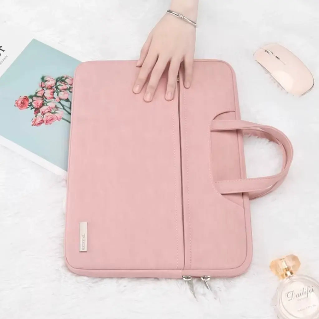 Sfeervolle opstelling met de laptoptas dames klein roze naast een roze muis, tijdschrift met bloemen en parfumflesje. Een hand rust licht op de tas, wat het gebruiksgemak en de aantrekkelijke vormgeving van dit functionele mode-accessoire benadrukt.