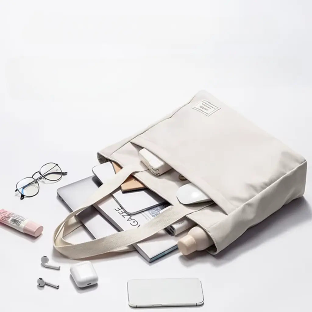 Laptoptas fashion 14 inch van crèmekleurig canvas gevuld met laptop, tijdschriften, smartphone en accessoires, toont de ruime capaciteit.