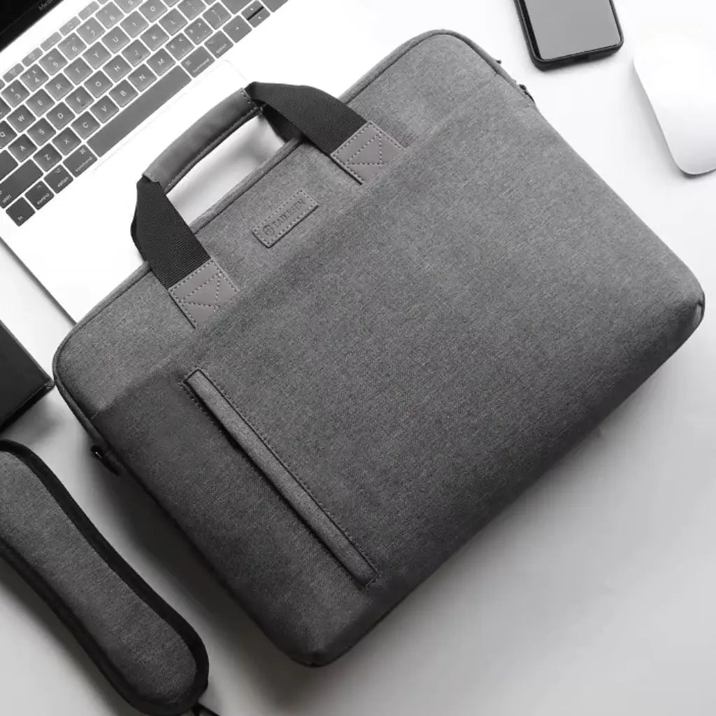 Een laptoptas heren 17 inch grijs donkergrijs op een wit bureau naast een laptop en smartphone, met zichtbare zwarte handgrepen en een praktisch voorvak voor snelle toegang tot documenten.