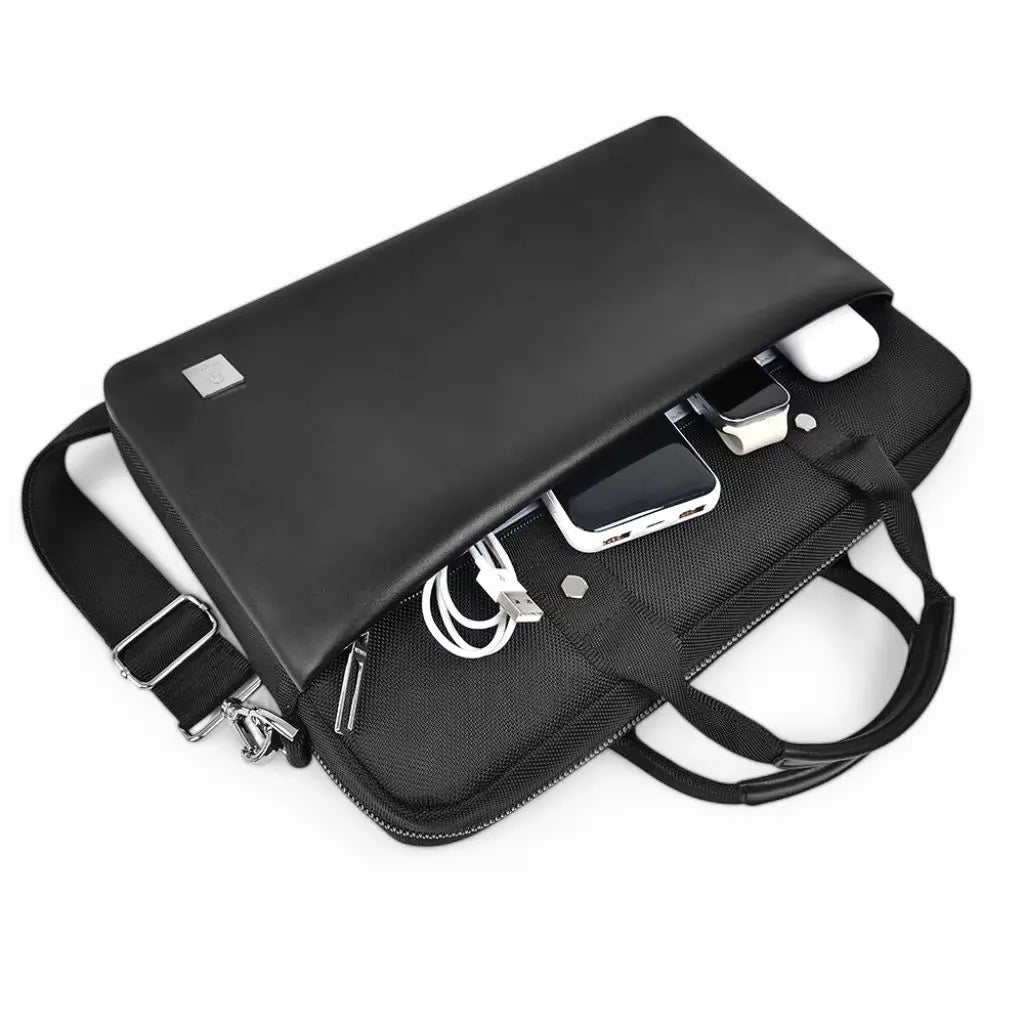Een stijlvolle leren laptoptas dames zwart die open ligt en gevuld is met verschillende accessoires. De tas heeft meerdere vakken om kabels, adapters, een mobiele telefoon, USB-sticks en andere accessoires georganiseerd te houden. De laptoptas combineert een elegant leren ontwerp met praktische functionaliteit voor dagelijks gebruik.