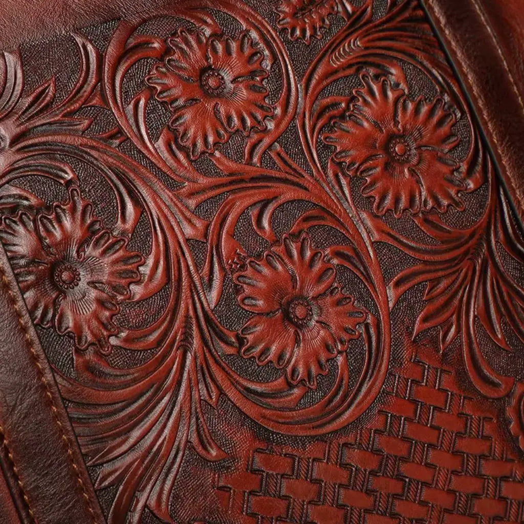 Detailopname van het gegraveerde bloemmotief op de leren vintage laptoptas dames 14 inch bruin. Het kunstige handwerk toont prachtige bloemen en gevlochten patroon in het hoogwaardige bruinrode leer, wat de ambachtelijke kwaliteit van deze laptoptas benadrukt.
