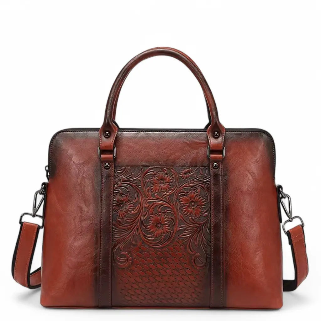 Elegante leren vintage laptoptas dames 14 inch bruin met gegraveerde bloemmotieven, handvatten aan de bovenkant en een afneembare schouderriem. De luxe bruinrode leren tas is voorzien van kunstig bewerkte details en biedt voldoende ruimte voor een laptop.