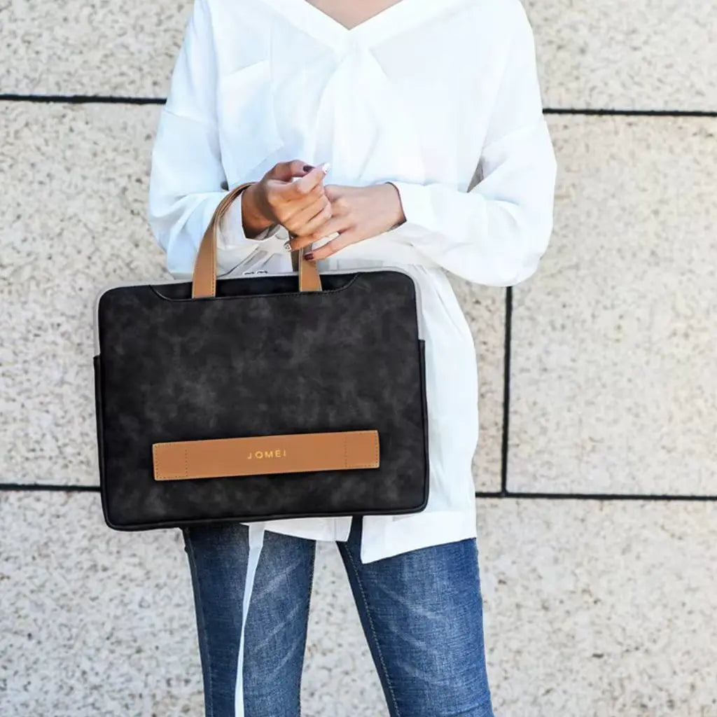 Vrouw in witte blouse en jeans draagt een mooie laptoptas dames 17 inch zwart met bruine leren accenten, een praktische en stijlvolle keuze voor dagelijks zakelijk gebruik.