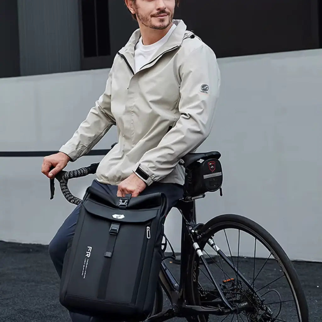Man met lichte jas op een fiets met een zwarte Nomad laptop rugzak, perfect voor dagelijks woon-werkverkeer in de stad.