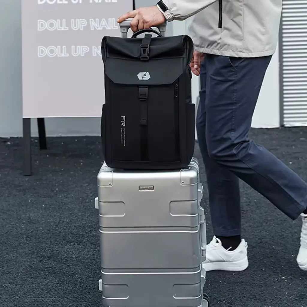 Man met Nomad laptop rugzak bovenop zilverkleurige koffer, ideale combinatie voor zakenreizen en flexwerken.