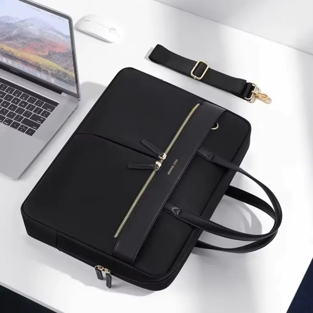 Bovenaanzicht van leuke laptoptas dames 15.6 inch zwart met afneembare schouderriem, naast een MacBook op een witte bureau-opstelling, perfect voor dagelijks gebruik.