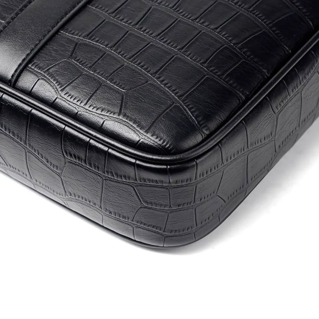 Close-up van de textuur van de stoere leren laptoptas 13 inch. Het zwarte krokodillenleerpatroon toont de gedetailleerde reliëfafwerking en nauwkeurige stiksels die de duurzaamheid en premium kwaliteit van deze laptoptas benadrukken.