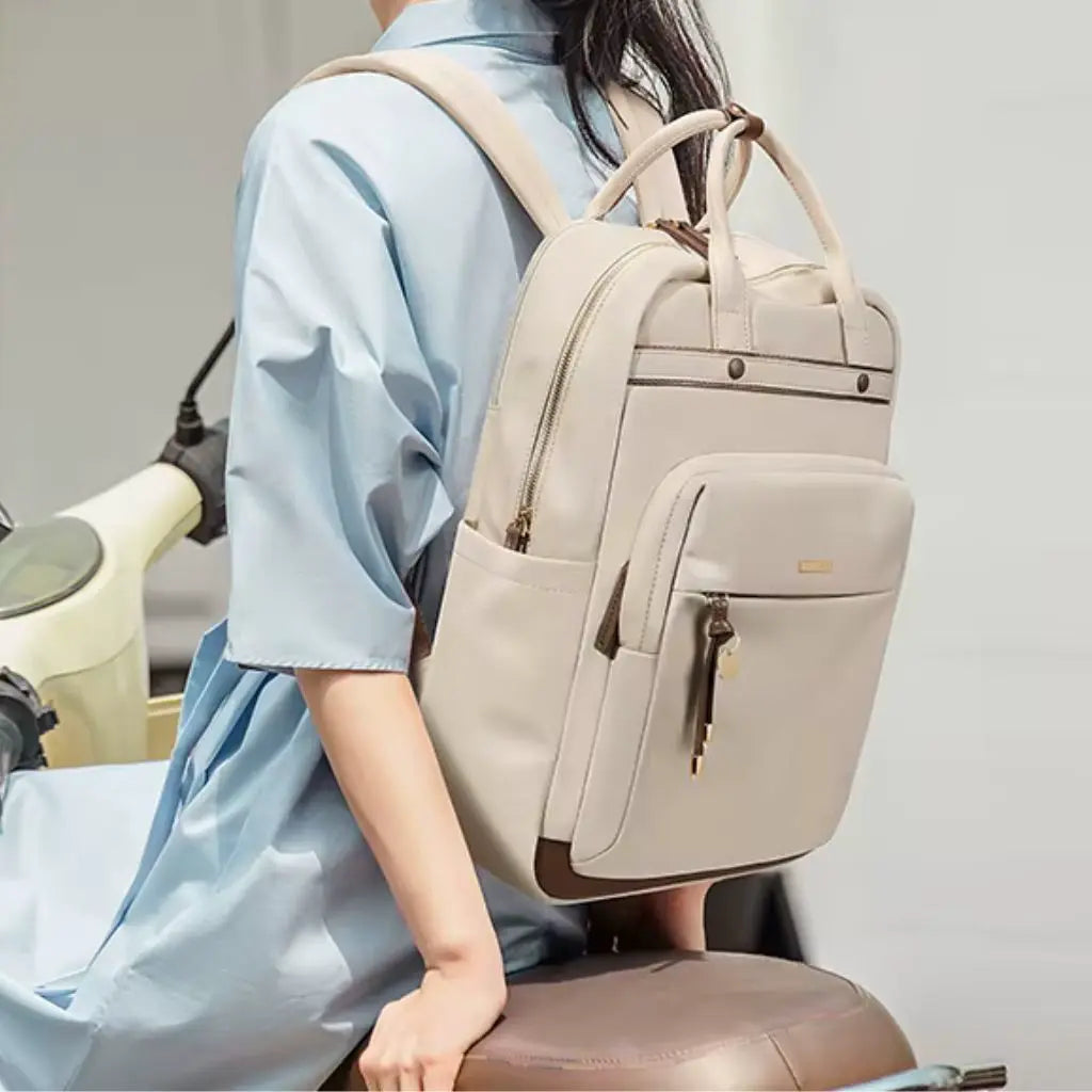 Een model draagt de waterdichte laptop rugzak 15.6 inch beige op de rug, wat het draagcomfort en de pasvorm demonstreert. De rugzak past stijlvol bij de lichtblauwe outfit en laat zien hoe de tas comfortabel op de rug zit tijdens het dragen. Perfect voor dagelijks gebruik naar kantoor of studie.