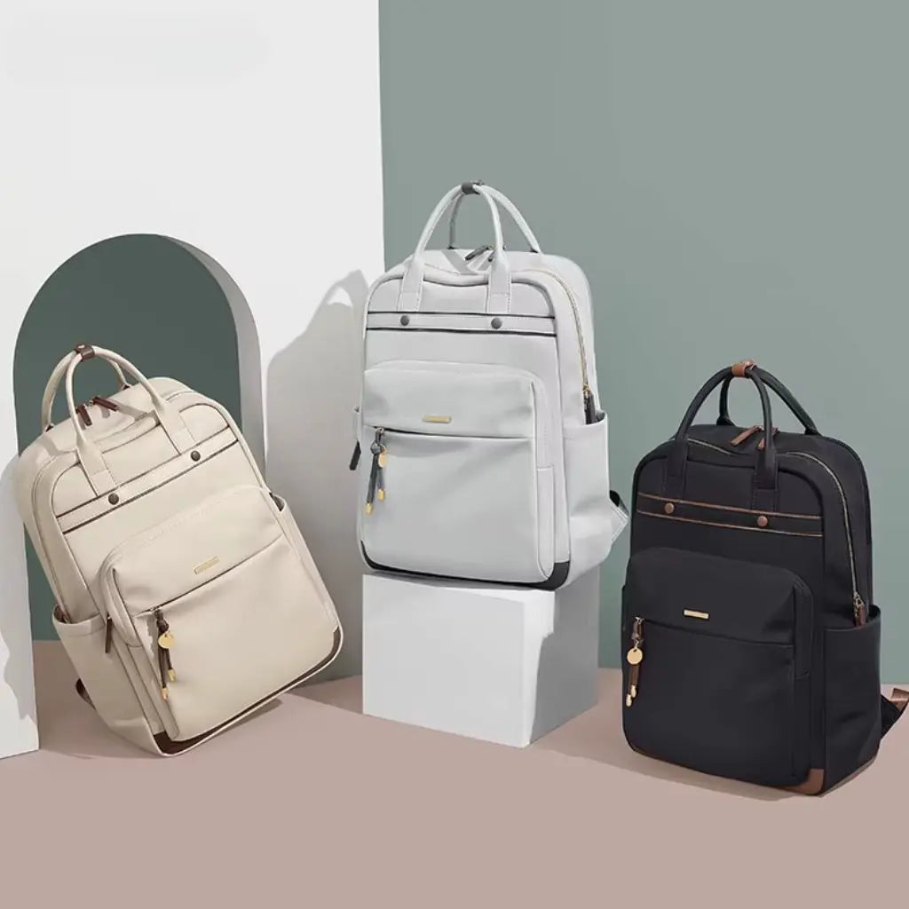 Een collectie van drie waterdichte laptop rugzakken in verschillende kleuren, waaronder een waterdichte laptop rugzak 15.6 inch zwart aan de rechterkant. De beige en grijze modellen hebben hetzelfde design als het zwarte model, met metalen knoppen, voorvakken en decoratieve hangers. Deze stijlvolle rugzakken zijn elegant gepresenteerd tegen een minimalistische achtergrond met zachtgroene accenten.