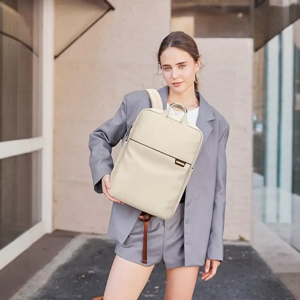 Vrouw in grijs pak die een beige waterdichte laptop rugzak 17 inch draagt, demonstreert de stijlvolle uitstraling en elegante pasvorm, perfect voor zakelijke professionals en moderne forensen.