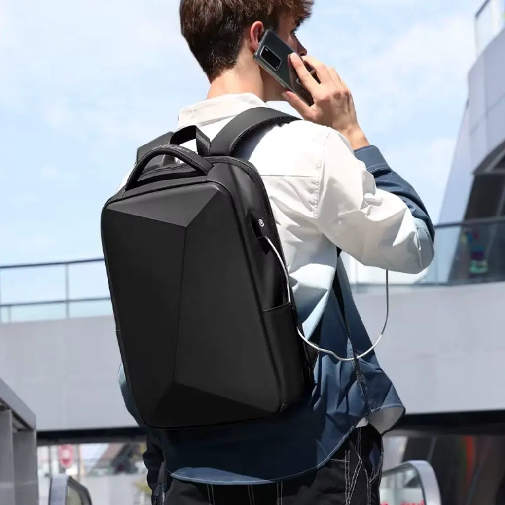 Man in zakelijke kleding met een zwarte waterdichte laptop rugzak heren 15.6 inch op zijn rug, telefonerend terwijl hij een oortje gebruikt dat is aangesloten op de USB-poort van de rugzak.