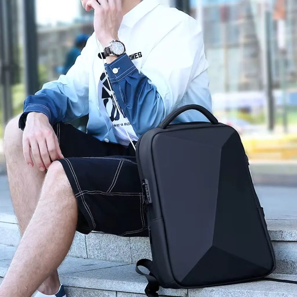 Jonge man zittend met zijn zwarte waterdichte laptop rugzak heren 15.6 inch naast hem, gekleed in een casual outfit met ombre overhemd, demonstreert de compacte maar ruime vorm van de tas.